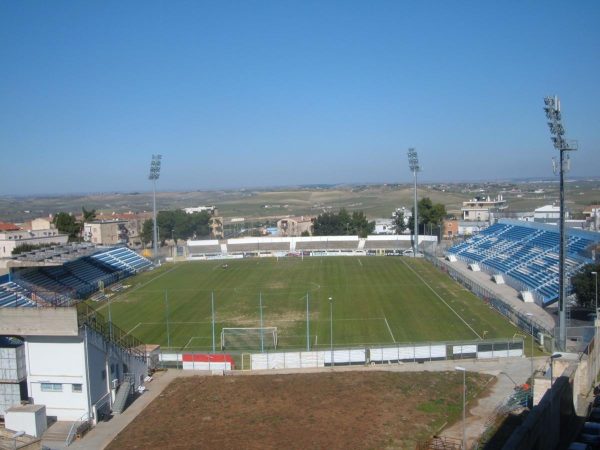 Il campo e le tribune con i seggiolini blu, visti dall'alto di una curva.